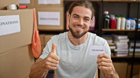Téléchargez les photos : Jeune homme hispanique faisant un geste pouce levé tenant du papier bénévole au centre de bienfaisance - en image libre de droit
