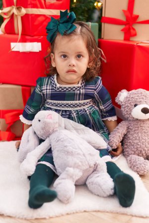 Foto de Adorable niño rubio sentado en el suelo por regalos de Navidad con expresión relajada en casa - Imagen libre de derechos