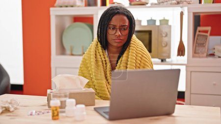 Foto de Mujer afroamericana teniendo consulta médica en línea sentada sobre la mesa estando enferma en el comedor - Imagen libre de derechos