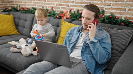 Téléchargez les photos : Père et fils célébrant Noël jouer avec des jouets à l'aide d'un ordinateur portable à la maison - en image libre de droit