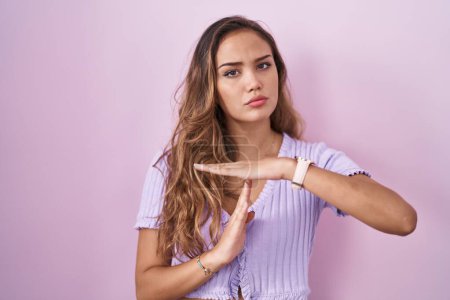Foto de Joven mujer hispana de pie sobre fondo rosa haciendo un gesto de tiempo fuera con las manos, rostro frustrado y serio - Imagen libre de derechos