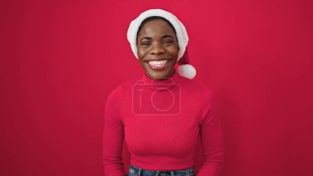 Photo for African american woman smiling confident wearing christmas hat over isolated red background - Royalty Free Image