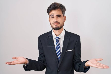 Photo for Young hispanic man with tattoos wearing business suit and tie clueless and confused with open arms, no idea concept. - Royalty Free Image