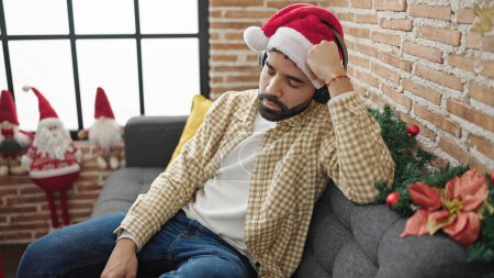 Téléchargez les photos : Jeune homme hispanique dormant sur le canapé portant un chapeau de Noël à la maison - en image libre de droit
