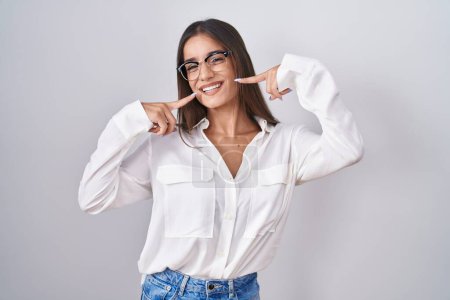 Téléchargez les photos : Jeune femme brune portant des lunettes souriantes et joyeuses montrant et pointant du doigt les dents et la bouche. concept de santé dentaire. - en image libre de droit