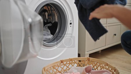 Photo for Young hispanic man washing clothes at laundry room - Royalty Free Image