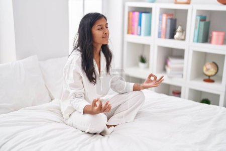Photo for Young beautiful hispanic woman doing yoga exercise sitting on bed at bedroom - Royalty Free Image