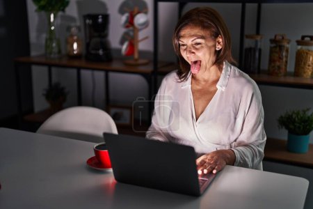 Photo for Middle age hispanic woman using laptop at home at night sticking tongue out happy with funny expression. emotion concept. - Royalty Free Image