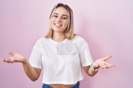 Photo for Young blonde woman standing over pink background smiling cheerful offering hands giving assistance and acceptance. - Royalty Free Image
