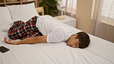 Foto de Joven hispano agotado capturado en un estado relajado, cómodamente acostado en una cama acogedora durmiendo tranquilamente en la tranquila mañana, un retrato de relajación en casa en el interior de un dormitorio - Imagen libre de derechos