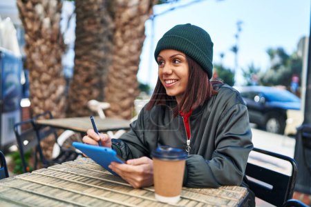 Photo for Young beautiful hispanic woman using touchpad drinking coffee at coffee shop terrace - Royalty Free Image