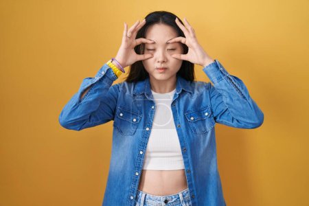 Téléchargez les photos : Jeune femme asiatique debout sur fond jaune essayant d'ouvrir les yeux avec les doigts, somnolent et fatigué pour la fatigue du matin - en image libre de droit