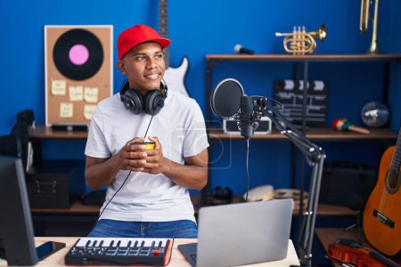 Téléchargez les photos : Jeune homme latin musicien ayant dj session boire du café au studio de musique - en image libre de droit