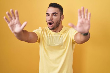 Téléchargez les photos : Jeune homme hispanique debout sur fond jaune faisant geste d'arrêt avec les paumes des mains, expression de colère et de frustration - en image libre de droit