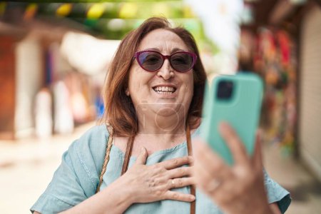 Foto de Mujer mayor turista sonriendo confiada teniendo videollamada en la calle - Imagen libre de derechos