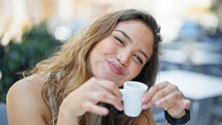 Téléchargez les photos : Jeune belle femme hispanique assise sur la table à boire du café souriant sur la terrasse du café - en image libre de droit
