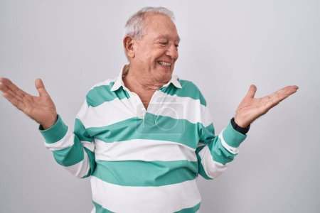 Téléchargez les photos : Homme âgé avec les cheveux gris debout sur fond blanc souriant montrant les paumes ouvertes des deux mains, présentant et comparant la publicité et l'équilibre - en image libre de droit