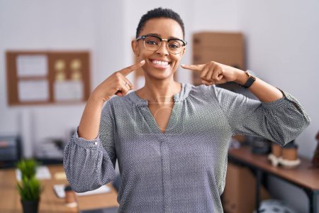 Téléchargez les photos : Femme afro-américaine travaillant au bureau portant des lunettes souriantes et joyeuses montrant et pointant du doigt les dents et la bouche. concept de santé dentaire. - en image libre de droit