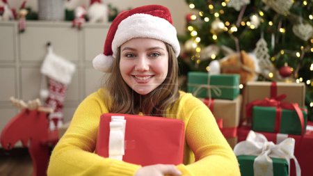 Foto de Joven mujer rubia sosteniendo regalo sentado en el suelo por el árbol de Navidad en casa - Imagen libre de derechos