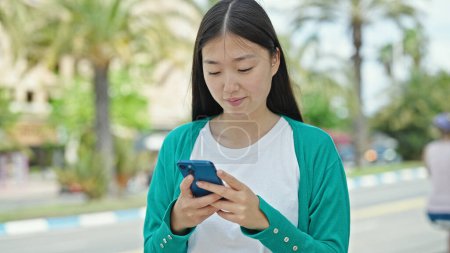 Téléchargez les photos : Jeune femme chinoise utilisant un smartphone avec expression gagnante dans la rue - en image libre de droit