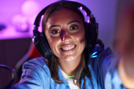 Foto de Young beautiful hispanic woman streamer smiling confident make selfie by camera at gaming room - Imagen libre de derechos