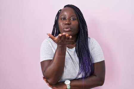 Téléchargez les photos : Jeune femme africaine debout sur fond rose regardant la caméra souffler un baiser avec la main sur l'air étant belle et sexy. expression d'amour. - en image libre de droit