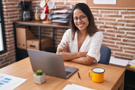 Photo for Young hispanic woman business worker using laptop sitting with arms crossed gesture at office - Royalty Free Image