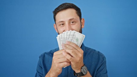 Photo for Young hispanic man smiling confident covering mouth with dollars over isolated blue background - Royalty Free Image
