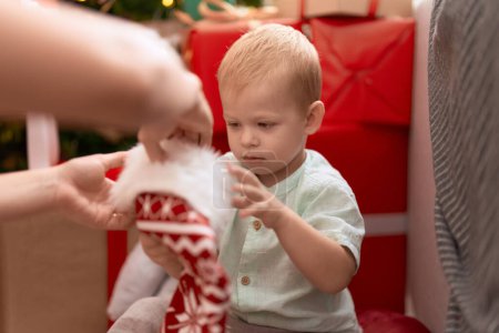 Photo for Adorable toddler sitting on floor by christmas gifts at home - Royalty Free Image