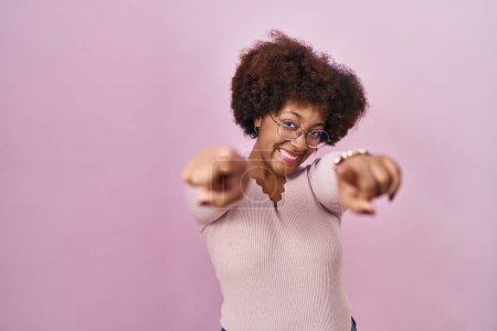 Photo for Young african american woman standing over pink background pointing to you and the camera with fingers, smiling positive and cheerful - Royalty Free Image