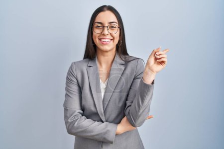 Photo for Hispanic business woman wearing glasses with a big smile on face, pointing with hand and finger to the side looking at the camera. - Royalty Free Image