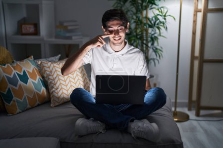 Photo for Young hispanic man using laptop at home at night pointing with hand finger to face and nose, smiling cheerful. beauty concept - Royalty Free Image
