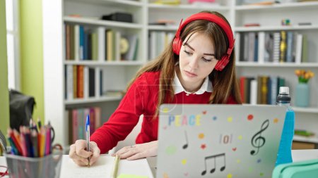 Téléchargez les photos : Jeune étudiante hispanique ayant des leçons en ligne d'écriture sur ordinateur portable à la bibliothèque de l'université - en image libre de droit