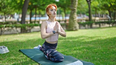 Photo for Young redhead woman training yoga exercise sitting on herb at park - Royalty Free Image