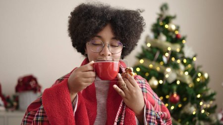 Foto de Mujer afroamericana joven desayunando de pie junto al árbol de Navidad en casa - Imagen libre de derechos