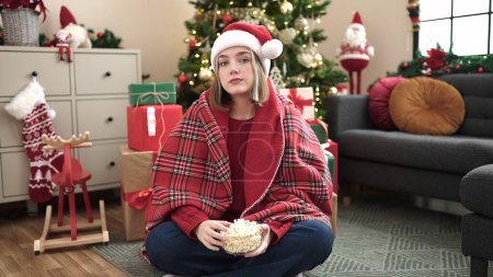 Foto de Mujer rubia joven viendo la película sentada en el suelo por el árbol de Navidad en casa - Imagen libre de derechos
