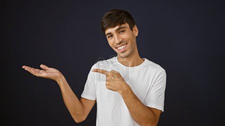 Téléchargez les photos : Jeune homme hispanique souriant pointant vers le côté présentant sur fond noir isolé - en image libre de droit