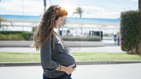 Téléchargez les photos : Jeune femme enceinte souriant confiant toucher le ventre au parc - en image libre de droit