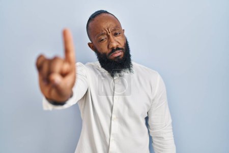 Téléchargez les photos : Homme afro-américain debout sur fond bleu pointant du doigt et l'expression en colère, ne montrant aucun geste - en image libre de droit