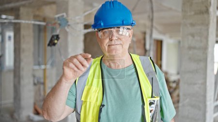 Téléchargez les photos : Moyen âge homme aux cheveux gris constructeur souriant confiant debout sur le chantier de construction - en image libre de droit