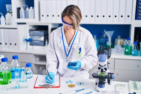 Photo for Young woman scientist writing report using smartphone at laboratory - Royalty Free Image