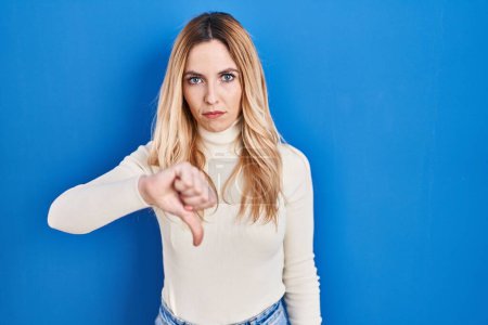 Photo for Young caucasian woman standing over blue background looking unhappy and angry showing rejection and negative with thumbs down gesture. bad expression. - Royalty Free Image