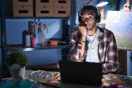 Photo for Young hispanic man sitting at art studio with laptop late at night looking stressed and nervous with hands on mouth biting nails. anxiety problem. - Royalty Free Image
