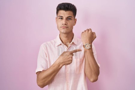 Téléchargez les photos : Jeune homme hispanique debout sur fond rose pressé pointant vers regarder le temps, l'impatience, regardant la caméra avec une expression détendue - en image libre de droit