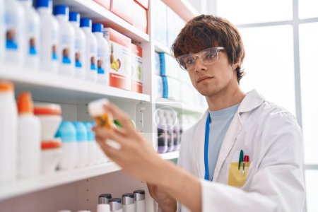 Photo for Young blond man pharmacist holding pills bottle at pharmacy - Royalty Free Image