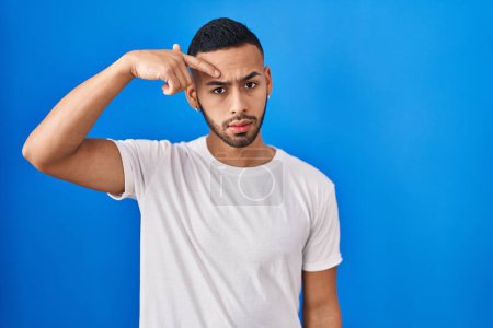 Photo for Young hispanic man standing over blue background pointing unhappy to pimple on forehead, ugly infection of blackhead. acne and skin problem - Royalty Free Image