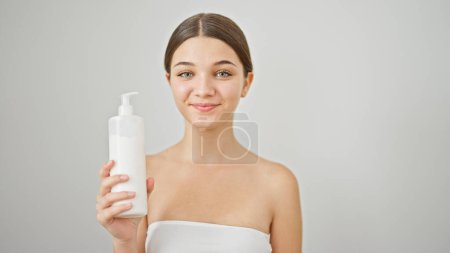 Téléchargez les photos : Jeune belle fille souriante confiante tenant bouteille de crème sur fond blanc isolé - en image libre de droit