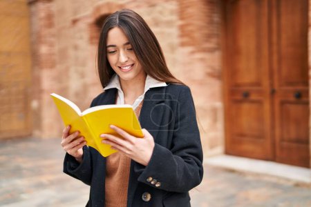 Photo for Young beautiful hispanic woman smiling confident reading book at street - Royalty Free Image