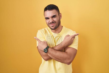 Téléchargez les photos : Jeune homme hispanique debout sur fond jaune pointant des deux côtés avec les doigts, direction différente en désaccord - en image libre de droit