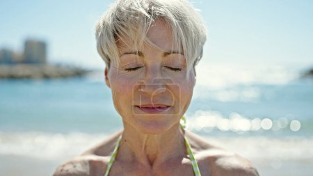 Téléchargez les photos : Moyen Age femme blonde touriste portant un bikini respirant à la plage - en image libre de droit